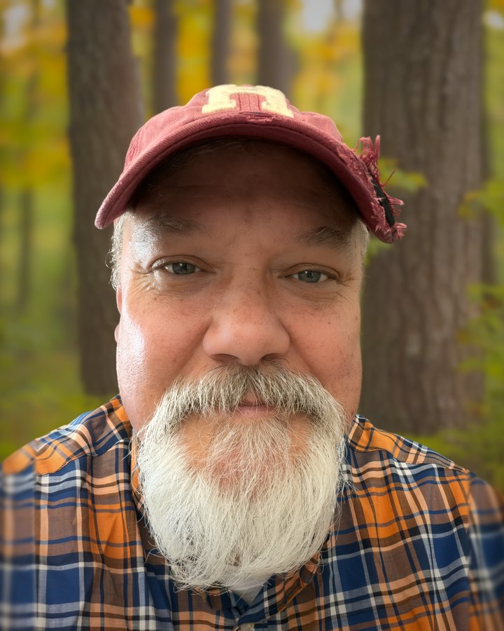 Tom Rankin today, in his red cap and plaid shirt, white beard, Ozark woods behind him.